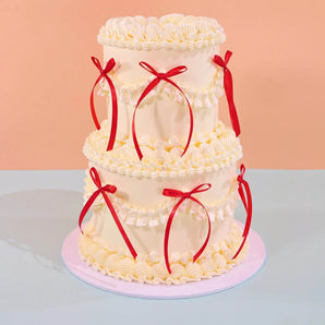 2 Tier Vintage Cake by Crumbs & Doilies with cream frosting and red ribbon decorations for parties and weddings